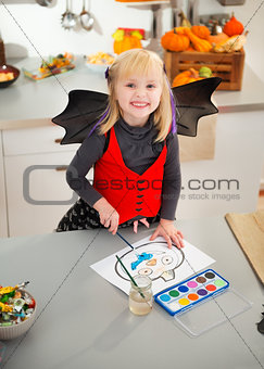Halloween dressed girl drawing pumpkin Jack-O-Lantern on paper