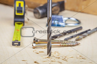Drill drilling into the wood with sawdust and tools around
