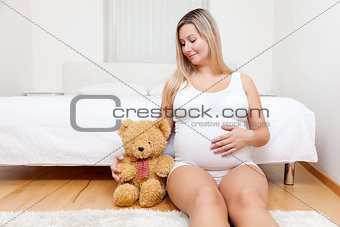 Young pregnant woman sitting on the floor with a teddy bear