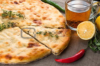 Top view of calzone pizza or chicken mushroom pie with pepper, lemon, rosemary and tea on linen fabric background