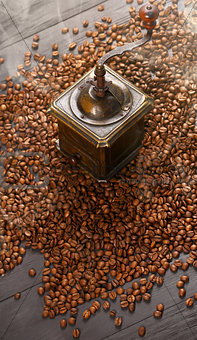 Old vintage coffee grinder on roasted hot beans with smoke