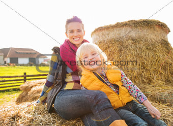 Portrait of beautiful woman and cute girl sitting on hay on farm