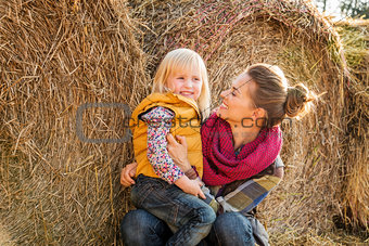 Portrait of woman and happy child sitting on hay on farm