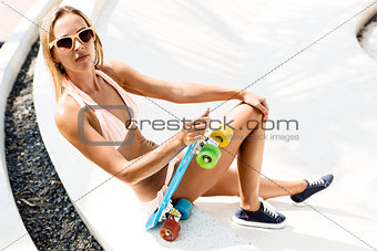 sexy suntanned lady sitting with blue penny board on the beach