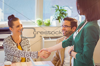 Casual business people shaking hands at desk and smiling