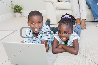 Happy siblings lying on the floor using laptop