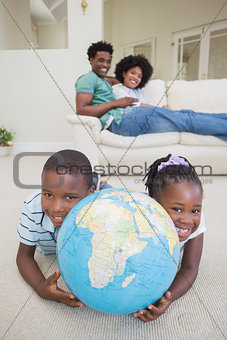 Happy siblings lying on the floor holding globe
