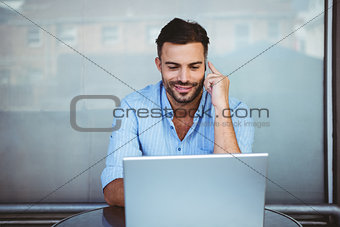 Smiling businessman on the phone working on laptop