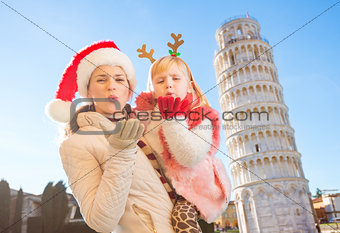Mother in Christmas hat and daughter giving air kiss in Pisa