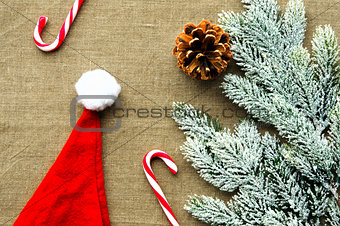 Christmas decorations: top view of candy canes, cones, Santa cap and pine branch on linen fabric background