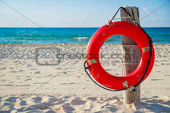 Life buoy on a pole on a sandy beach with blue ocean water