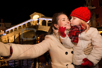 Daughter kissing mother taking selfie in Christmas Venice, Italy
