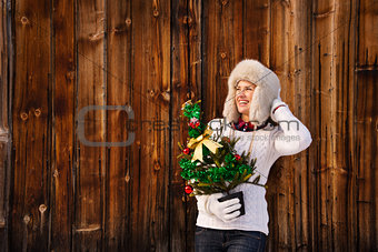Woman with Christmas tree near rustic wall looking copy space