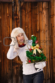 Happy woman holding Christmas tree and looking on something