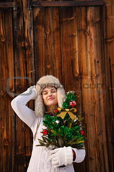 Relaxed woman with Christmas tree in front of rustic wood wall