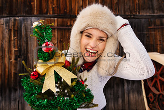 Young woman with Christmas tree in the front of rustic wood wall