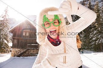 Woman in Christmas glasses framing with hands in the countryside