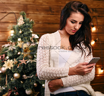 Attractive festive young woman  in front of the Xmas tree checking for Christmas messages on her mobile phone