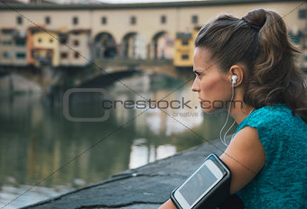 Young fitness female with mp3 player staying close to Arno river
