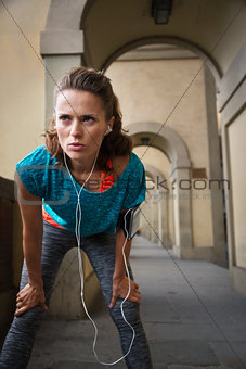 Sporty woman with earphones catching breath after jogging