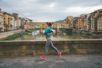 Young female jogger with headset is running by Arno riverside