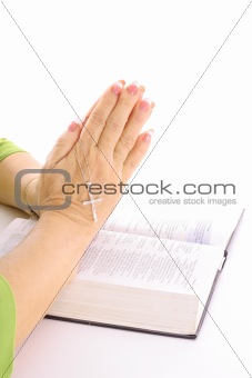 shot of praying hands over bible with rhinestone cross