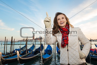 Woman traveler standing on embankment in Venice and pointing up