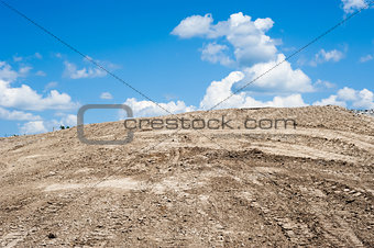 Sandy dirt hill with tracks against clouds and sky
