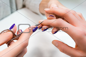 Manicure with scissors in nail salon