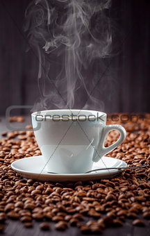 Hot aromatic coffee drink in the white cup with beans background
