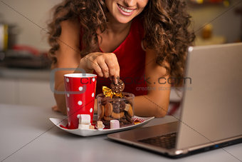 Woman having cup of hot chocolate with cookies and using laptop