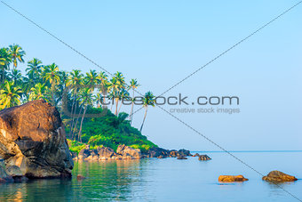 a large boulder in a calm sea and palm trees