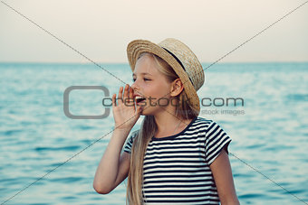 Young girl in a straw hat on the sea is calling someone