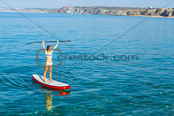 A beautiful and happy woman with arms up and learning paddle-sur