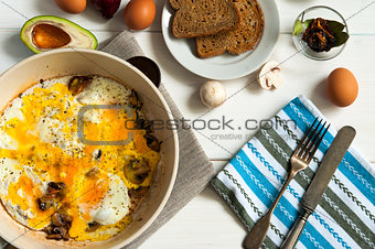 Hearty breakfast: plate of fried eggs and mushrooms with bread on white table surface, top view