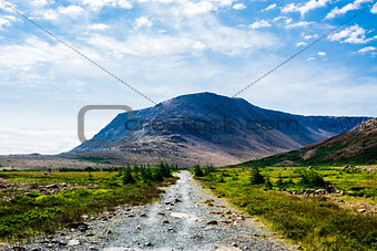 Rocky gravel path leading to mountain under clouds and sky