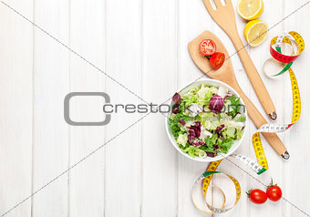 Fresh healthy salad, utensils and tape measure over white wooden