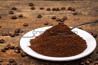 Ground coffee on white plate with sorrounding coffee beans