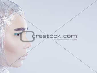 Profile of misterous pretty woman wrapped in cellophane looking forward standing on light grey background