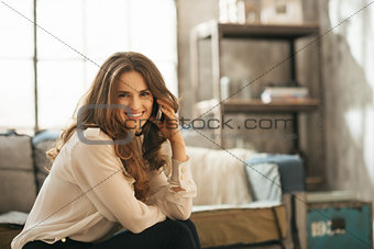 Smiling elegant woman sitting on sofa and talking smartphone