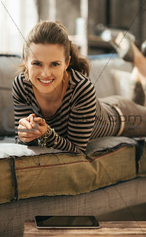 Smiling brown-haired stylish woman is laying down on sofa