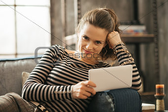 Portrait of young woman is laying on couch and holding tablet