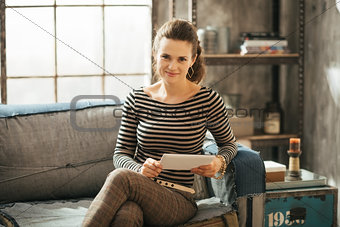 Young wealthy brunet woman sitting on couch and holding tablet