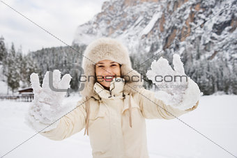 Woman in coat and fur hat showing snow-covered mittens outdoors