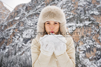Woman in fur hat blowing snow from hands in camera outdoors