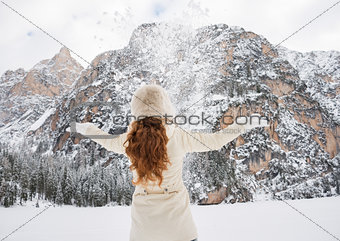 Seen from behind woman in coat and hat throwing snow outdoors