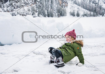 Happy child in green coat fell while playing in the snow.