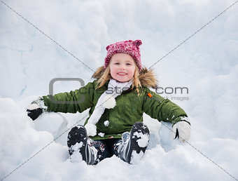 Happy child in green coat sitting on the snow