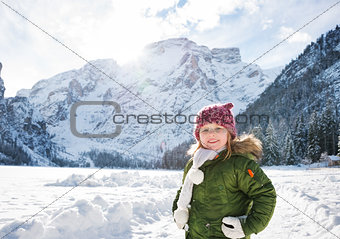 Happy child in green coat standing in front of snowy mountains