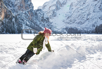 Child playing with the snow in the front of snowy mountains